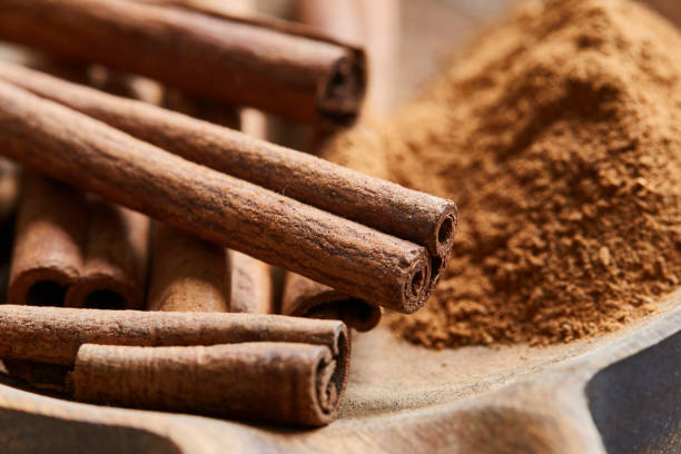 Cinnamon sticks and powder, macro shot Cinnamon sticks and powder in a handmade wooden bowl, on a kitchen table, baking preparation, macro shot with a copy space Cinnamon stock pictures, royalty-free photos & images