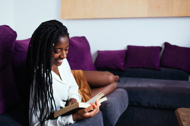 istock Cheerful dark skinned woman with braids smiling while read novel on free time in comfortable living room, pretty african american hipster girl lying on sofa enjoying educational literature on leisure 1449632518