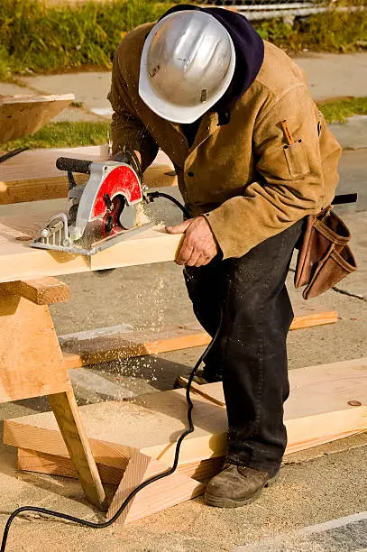 A construction worker cutting a piece of lumber with a circular saw to make a stair stringer