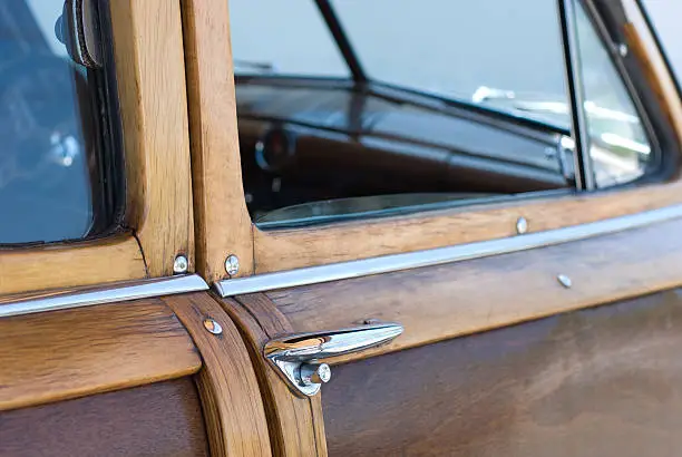 This photo depicts the door and chrome handle of an old woody vehicle.