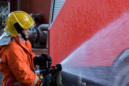 Fire man spray water from hose for fire fighting. Firefighter spraying a straight steam