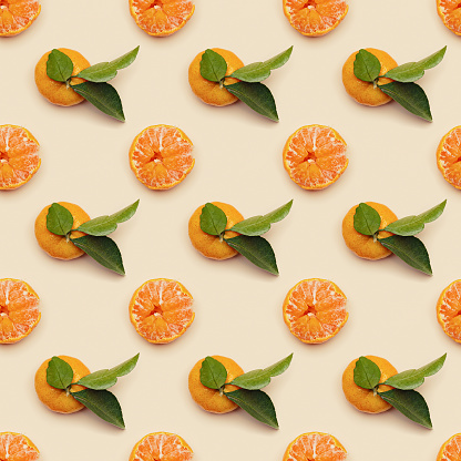 Orange yellow juicy tangerines with green leaves, whole and peeled on neutral beige background, seamless pattern. Citrus fruits mandarins, healthy fruits food concept, creative styled photo, top view
