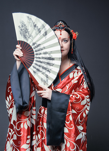 Beautiful young woman in red traditional Chinese costume with hand fan on dark background