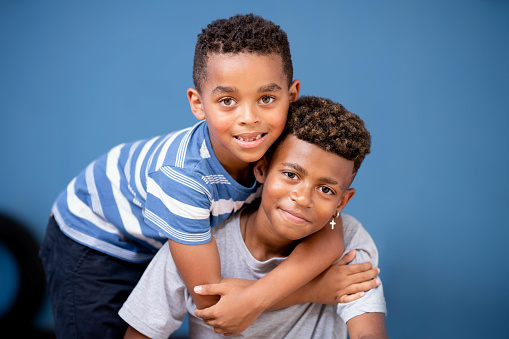 Portrait of a smiling young boy hugging his older brother while sitting together at home