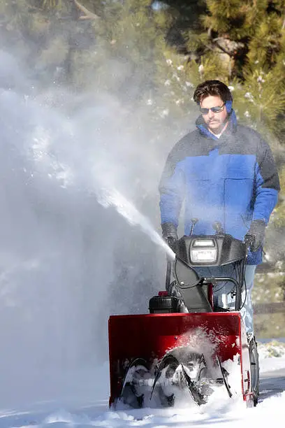 Man using a powerful snowblower to clear his driveway (shallow focus point on the snowblower machine).