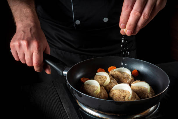 istock Cooking cutlets on grill pan by chef or cook hands on black background for copy space text restaurant menu. The chef adds salt 1449658190