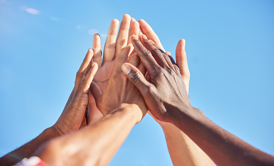 High five, sports and team with support, motivation and solidarity during a game with a blue sky. Group of people, athlete friends or men with hands together for a win, success and partnership