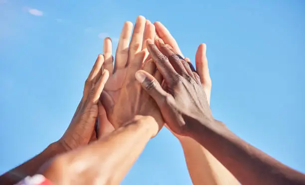 Photo of High five, sports and team with support, motivation and solidarity during a game with a blue sky. Group of people, athlete friends or men with hands together for a win, success and partnership