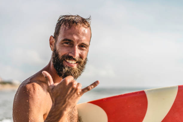 surfer zadowolony z surfowania z uśmiechem robi hawajski shaka brah lub hang loose podczas sesji surfingowej w falach oceanu na wakacjach na plaży - cel podróży surfingowych - przyjazne powitanie w kulturze surferów - co surfing zdjęcia i obrazy z banku zdjęć