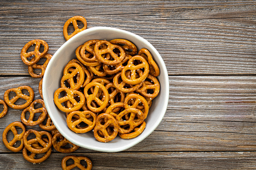 Party food: snack pretzels in a black bowl shot from above on white background. Predominant colors are gold and white. High resolution 42Mp studio digital capture taken with SONY A7rII and Zeiss Batis 40mm F2.0 CF lens