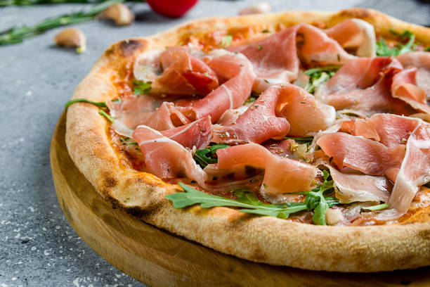 istock Pizza with Parma ham and arugula on wooden board on grey table macro close up 1449681409