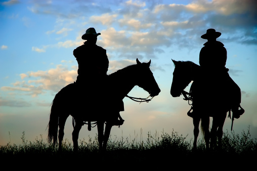 Cowboys on a Montana ridge at dawn, back lit by the rising sun