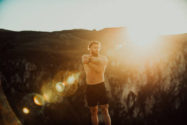 Male athlete doing arm stretching exercise on top of a mountain.