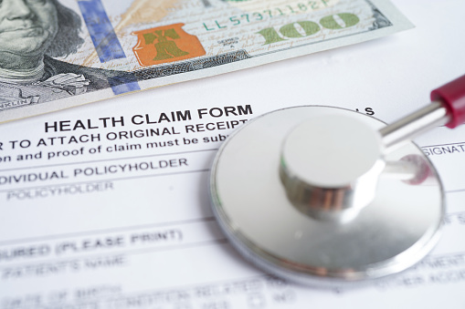 Health claim form with stethoscope and US dollar banknotes, insurance accident medical concept.