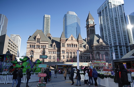 Toronto, Canada - December 4, 2022: Festival goers attend Holiday Fair in the Square, an annual Christmas celebration in Nathan Phillips Square. Background shows Toronto Old City Hall on Bay Street at Queen Street West. Sunny morning in the Yonge-Bay Corridor.