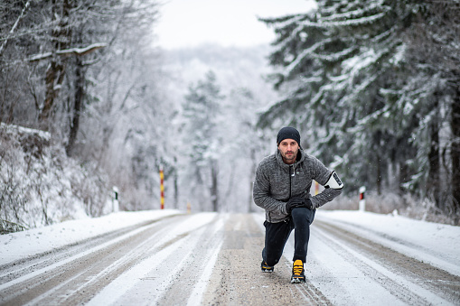 One man, an adult man exercises in the snowy forest in the fresh air, leads a healthy lifestyle, is dressed in sports clothes and does stretching and warm-up exercises