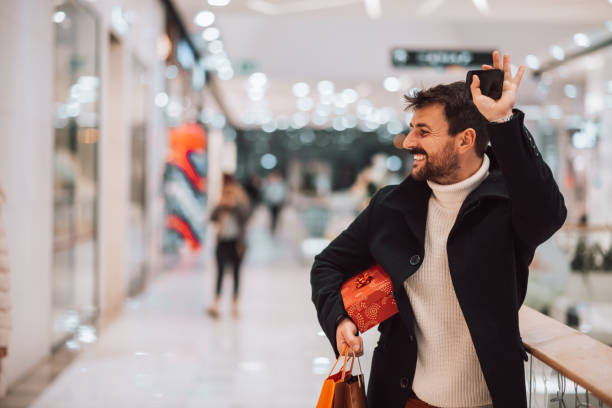 istock Attractive young man waving at the mall, holding shopping bags and a gift box 1449738708