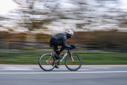 Black male cyclist riding through the Prospect park in Brooklyn, New York. He is wearing cycling gear, going for a training ride or commuting in style, on a sunny Autumn day.