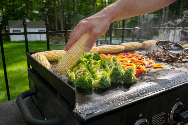Person grilling vegetables. Freshly grilled barbecue, corn, mushrooms, paper and broccoli.