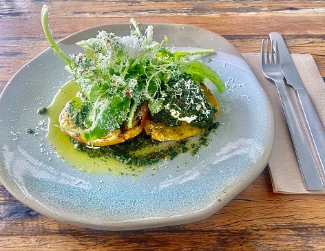 Horizontal flat lay high angle view of gourmet breakfast poached eggs with rocket basil pesto, parmesan cheese greens and haloumi on gluten free btoast on hand made plate ceramic placed on a distressed wood wood table in Mullumbimby cafe NSW Australia