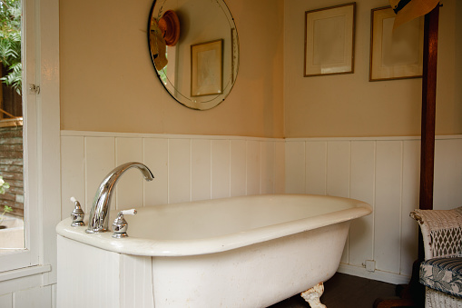 Vintage clawfoot cast iron bathtub in white and creme bathroom with wall decor and round mirror