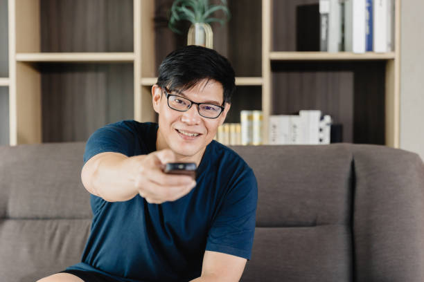 istock Man Happy Smile Pointing Tv Remote Control For Watching Home Entertainment Program At Holiday Weekend. 1449766281