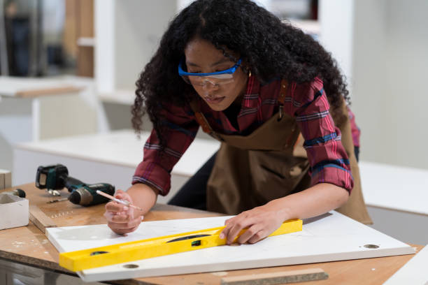 istock Woman carpenter using precision level making new furniture at carpentry workshop. Production line of the wooden factory 1449766402