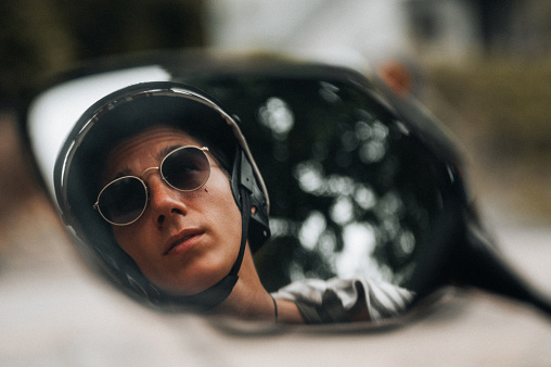 Young man driving a motorbike . He is wearing a helmet and sunglasses, enjoying his day, traveling solo through the beautiful nature of the islands in Thailand.
