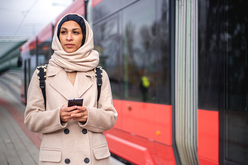Young muslim woman with smartphone coming out of a tram.
