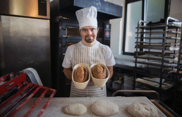 istock Young baker with down syndrome preparing pastries in bakery. Concept of integration people with disabilities into society. 1449773469