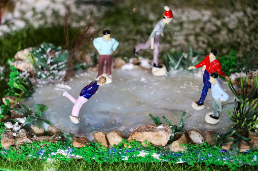 Seasonal concept photo showing a magical model Christmas village scene in winter set up in the living room of my house. The model village recreates a detailed winter's scene in miniature and comes complete with hand-painted people and scale figurines, tiny battery-powered fairy lights, a frozen pond with ice skaters, and lots of fake snow powder.