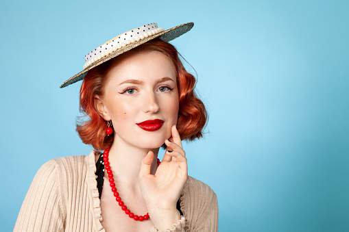 Studio portrait of a cheerful red-haired white woman dressed in retro style against a blue background