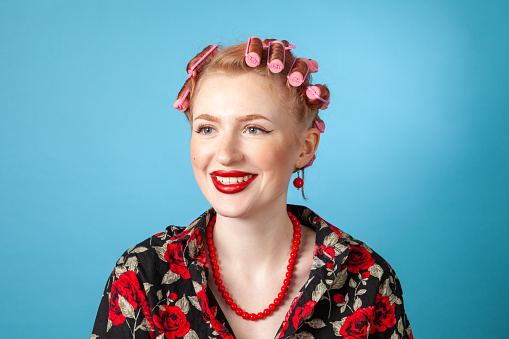 Studio portrait of a cheerful young white woman in pink curlers against a blue background