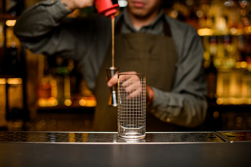 Front view of clean transparent empty glass with grid pattern on bar. Blurred male bartender at background