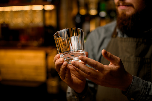 Focus on clean transparent shiny empty old-fashioned glass for drink in male bartender hands. Blurred background