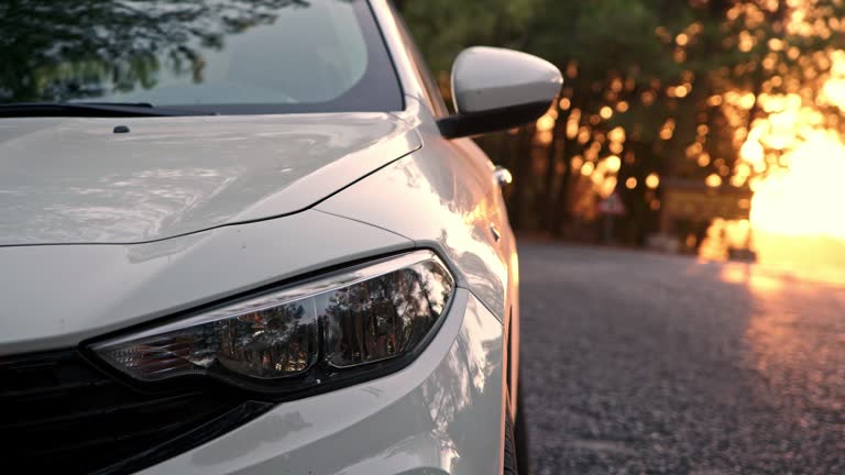 Close up view of front light of car headlights. unrecognizable white car is parked on side of road with setting sun in background. detail of exterior of modern car.