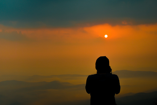 Young man standing and taking pictures of misty sea view Surrounded by mountains, Silhouettes in the sunset.