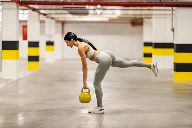 A strong sportswoman is balancing on on foot and lifting kettle bell ripl fitness
