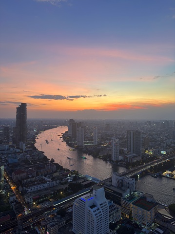 Bangkok Cityscape in moody colorful sunset light. High angle view along the Chao Phraya River into the setting sun at dusk. Bangkok, Thailand, Southeast Asia