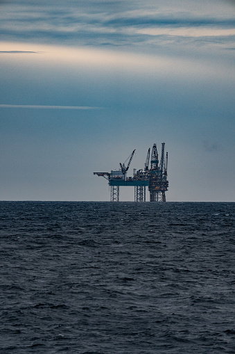 A deep water oil drilling platform at sea with calm waters and cumulus clouds against blue sky. 