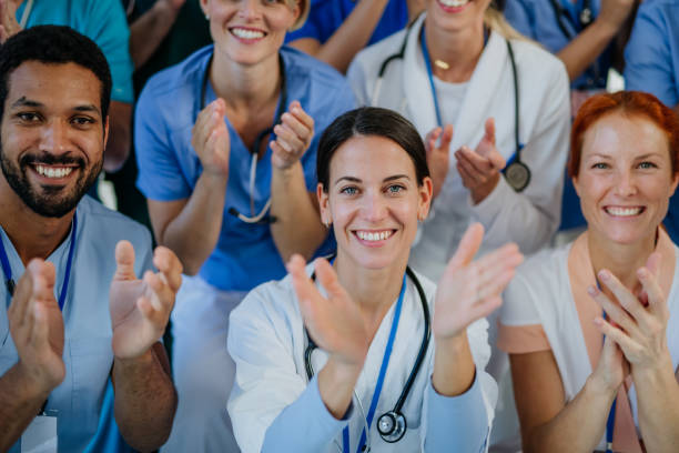 Portrait of happy doctors, nurses and other medical staff clapping in hospital. stock photo