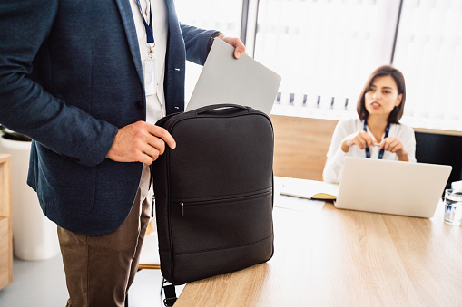 An unrecognizable businessman at his workplace, putting laptop into backpack.