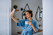 Young woman taking selfie in bathroom, enjoying cup of coffee.