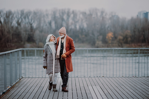 Elegant senior couple walking near a river, during cold winter day.