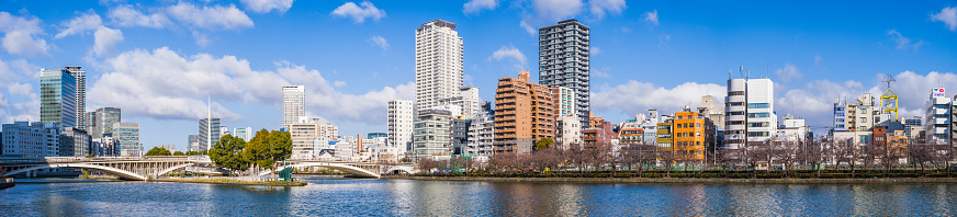 Crowded high-rise cityscape of hotels, apartment buildings and offices reflecting in the tranquil waters of the Kyu-Yodo River in central Osaka, Japan.