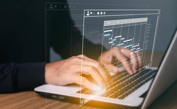 istock Project manager working on laptop and updating tasks and milestones progress planning with Gantt chart scheduling interface for company on virtual screen. 1449822195