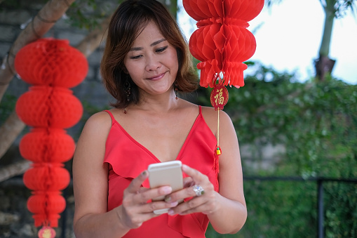 Close-up shot of mature Chinese woman using phone, text messaging her family and friends during Chinese new year.