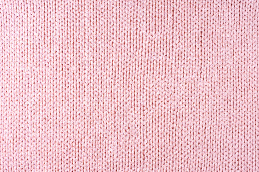 Close up background of knitted wool fabric made of viscose yarn. Pastel pink color wool knitwear texture. Abstract knitted jersey background. Fabric abstract backdrop, wallpaper