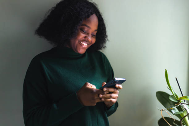istock Black woman texting beside window 1449825690