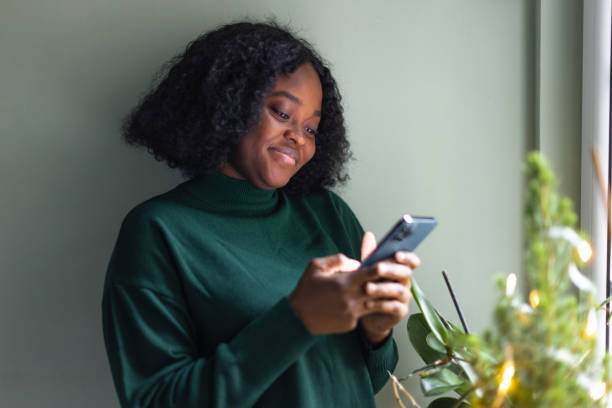 istock Black woman texting beside window 1449825719